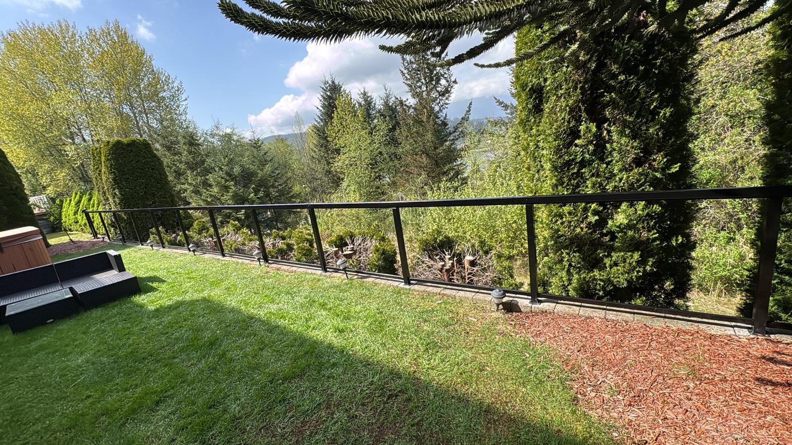 Glass railing along the edge of a sloped backyard in Port Moody