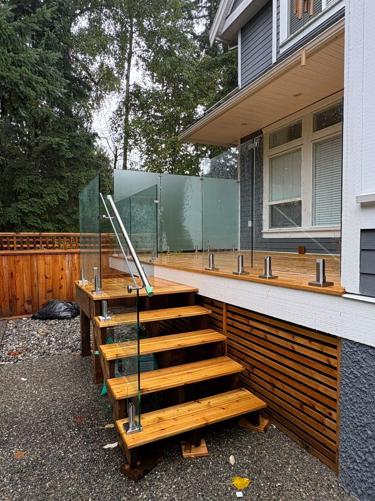 Clear glass stair railing with a handrail on cedar deck stairs in South Surrey